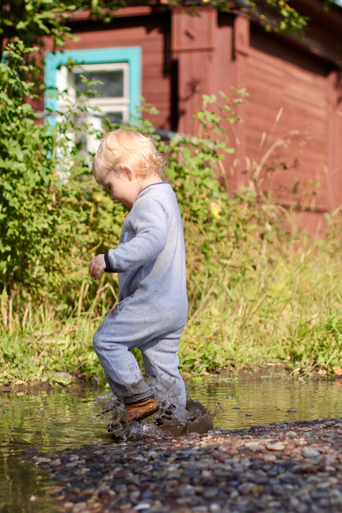 two year old boy in grey jumpsuit and brown leather boots running around the puddles, childhood